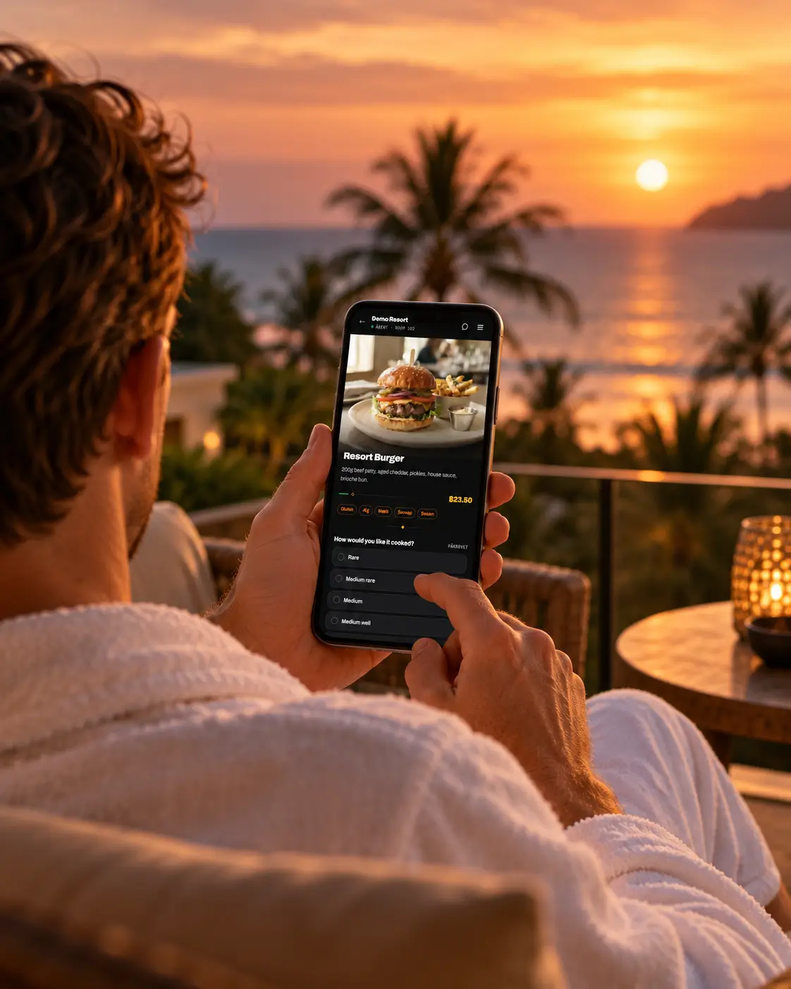 A guest in a bathrobe on a sea-view balcony at sunset, browsing the menu on their phone